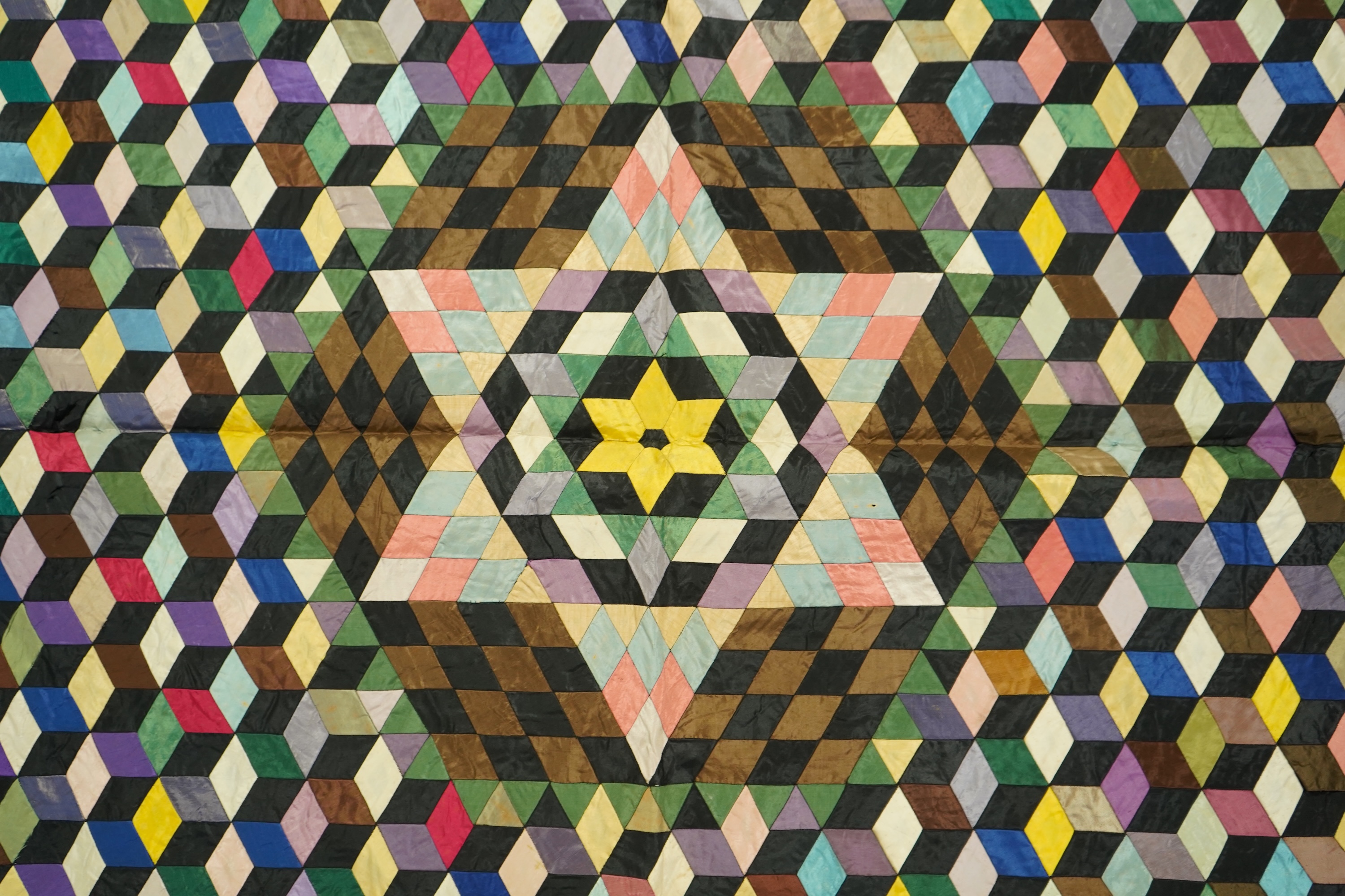 An English 19th century silk ‘Tumbling Blocks’, hand sewn, patchwork quilt, with central star motif and wide velvet border. Worked with multi coloured silks backed with black and blue silk., 170cm x 152cm. Condition - th